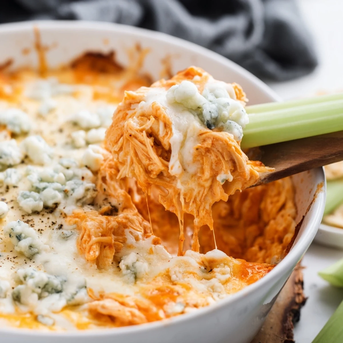 A close-up of creamy Spicy Buffalo Chicken Dip in a baking dish with celery sticks. 