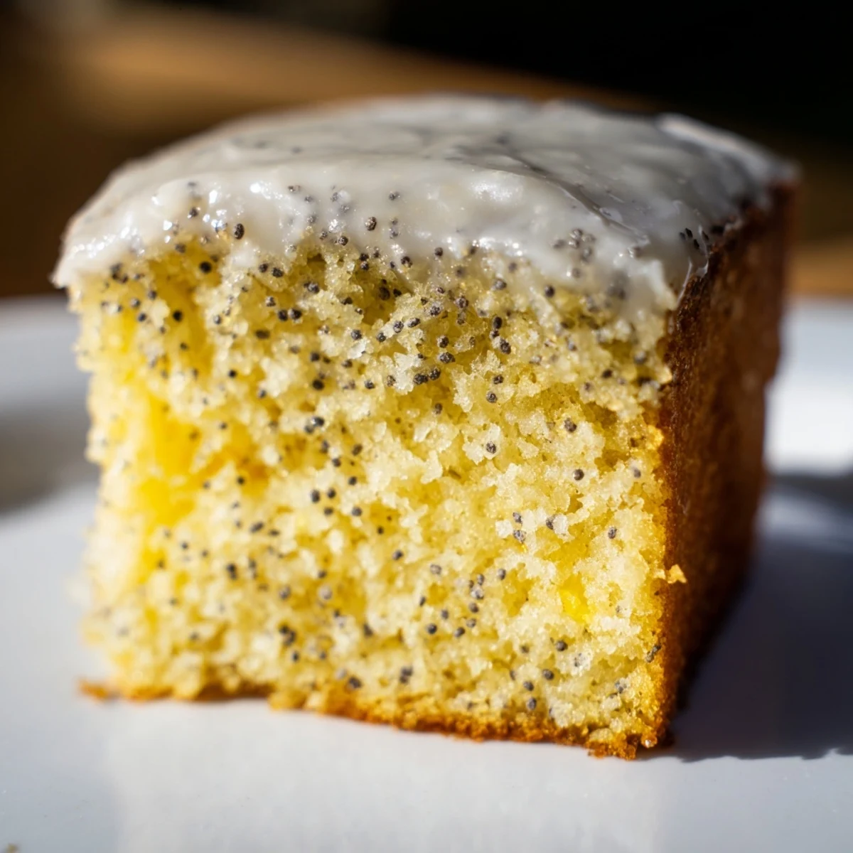 A close-up of glazed Lemon Drizzle Traybake with Poppy Seeds squares, showcasing a moist crumb with zesty lemon aroma.