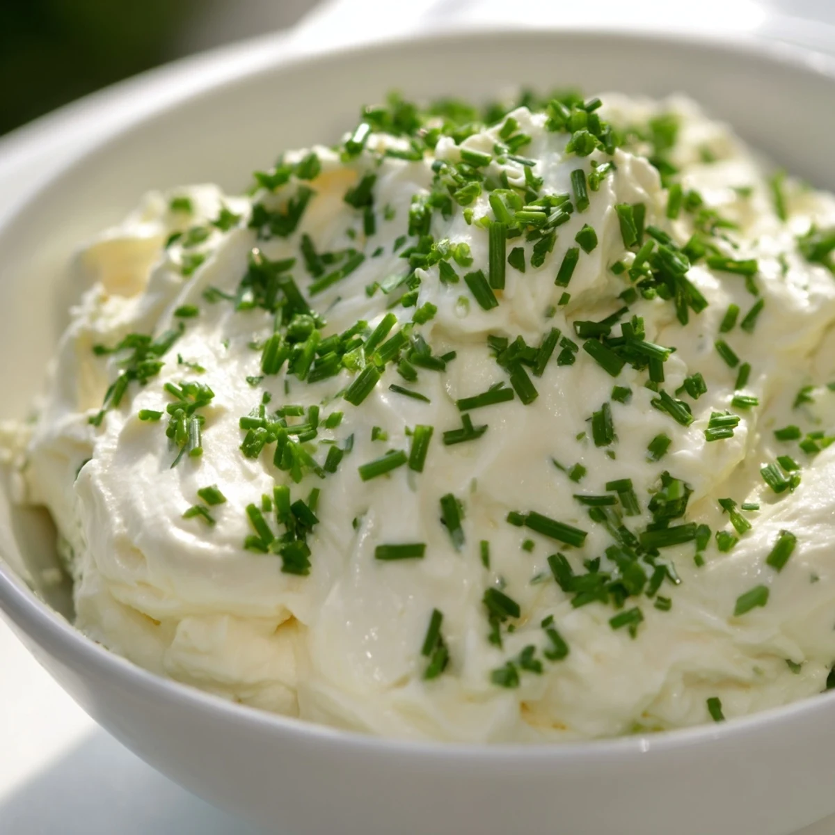 A close-up of Creamy Snack Dip in a white bowl, topped with herbs and paired with colorful fresh vegetables.