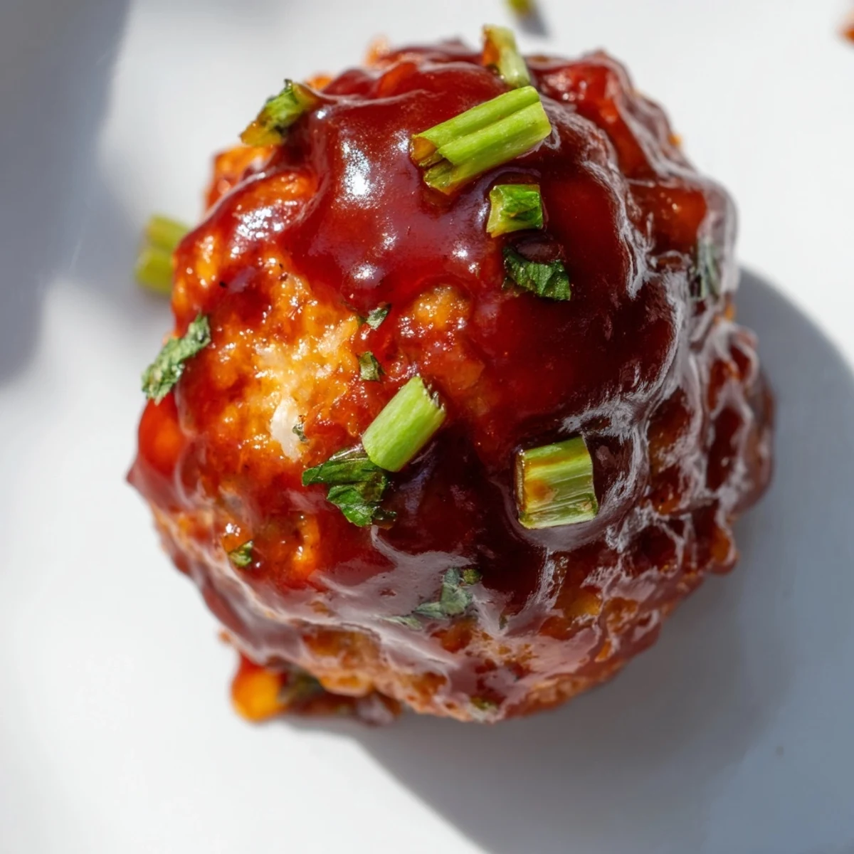 Golden-baked turkey appetizer meatballs glistening with sticky barbecue glaze and fresh parsley garnish on a white platter.