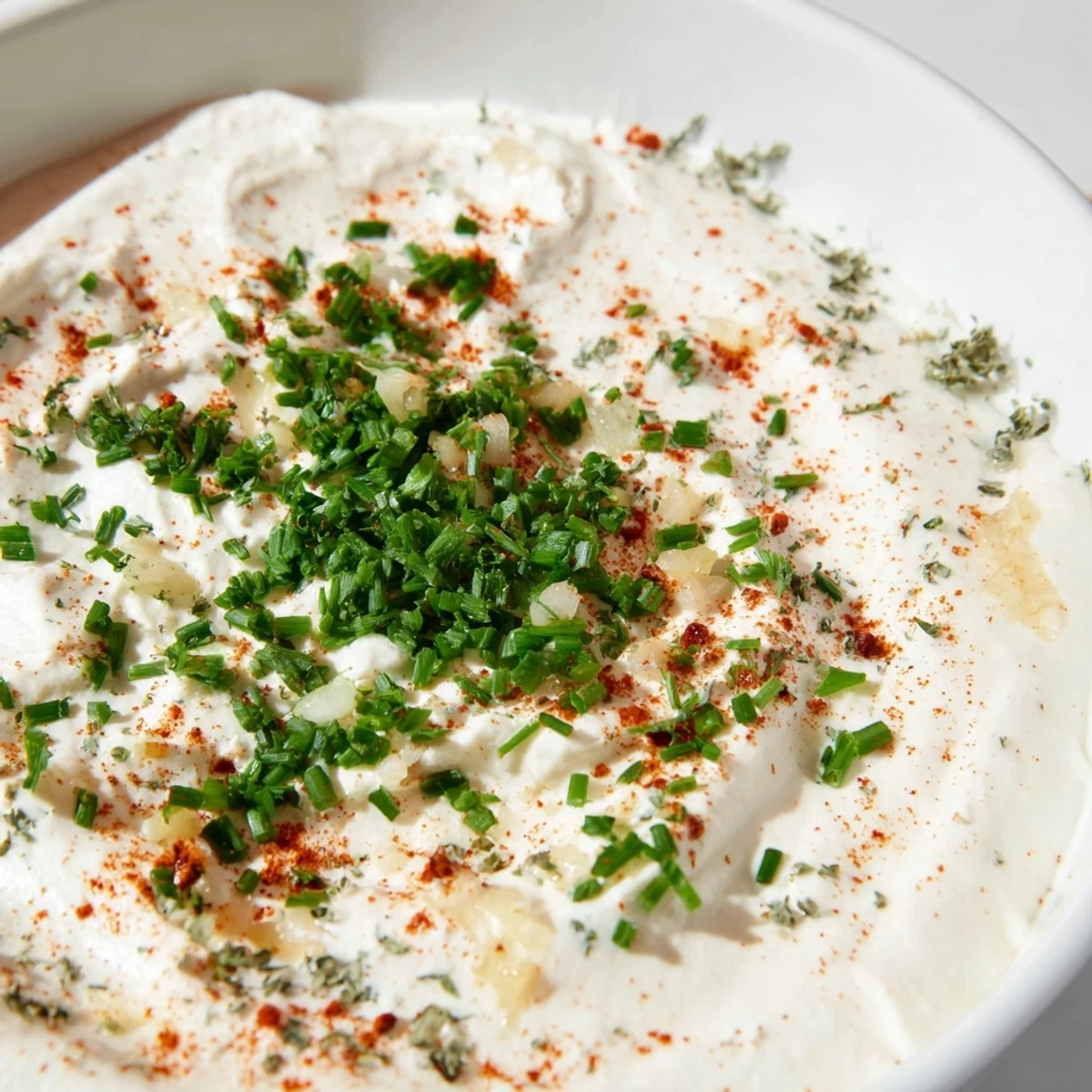 A bowl of Creamy Appetizer Dip topped with fresh chives and paprika, surrounded by crunchy vegetables and crackers.