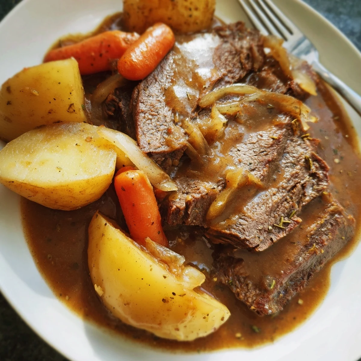 Sliced Slow Cooker Pot Roast with Carrots and Potatoes on a white plate, drizzled with savory gravy and fresh thyme garnish.