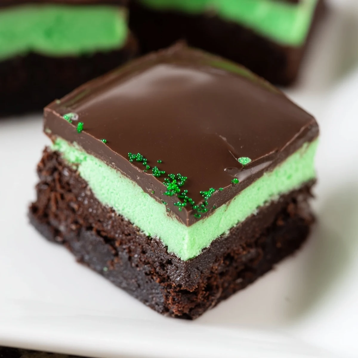 A close-up view of St. Patricks Day Mint Brownies cut into squares, showcasing the fudgy chocolate layers, vibrant mint frosting, and glossy ganache topping.