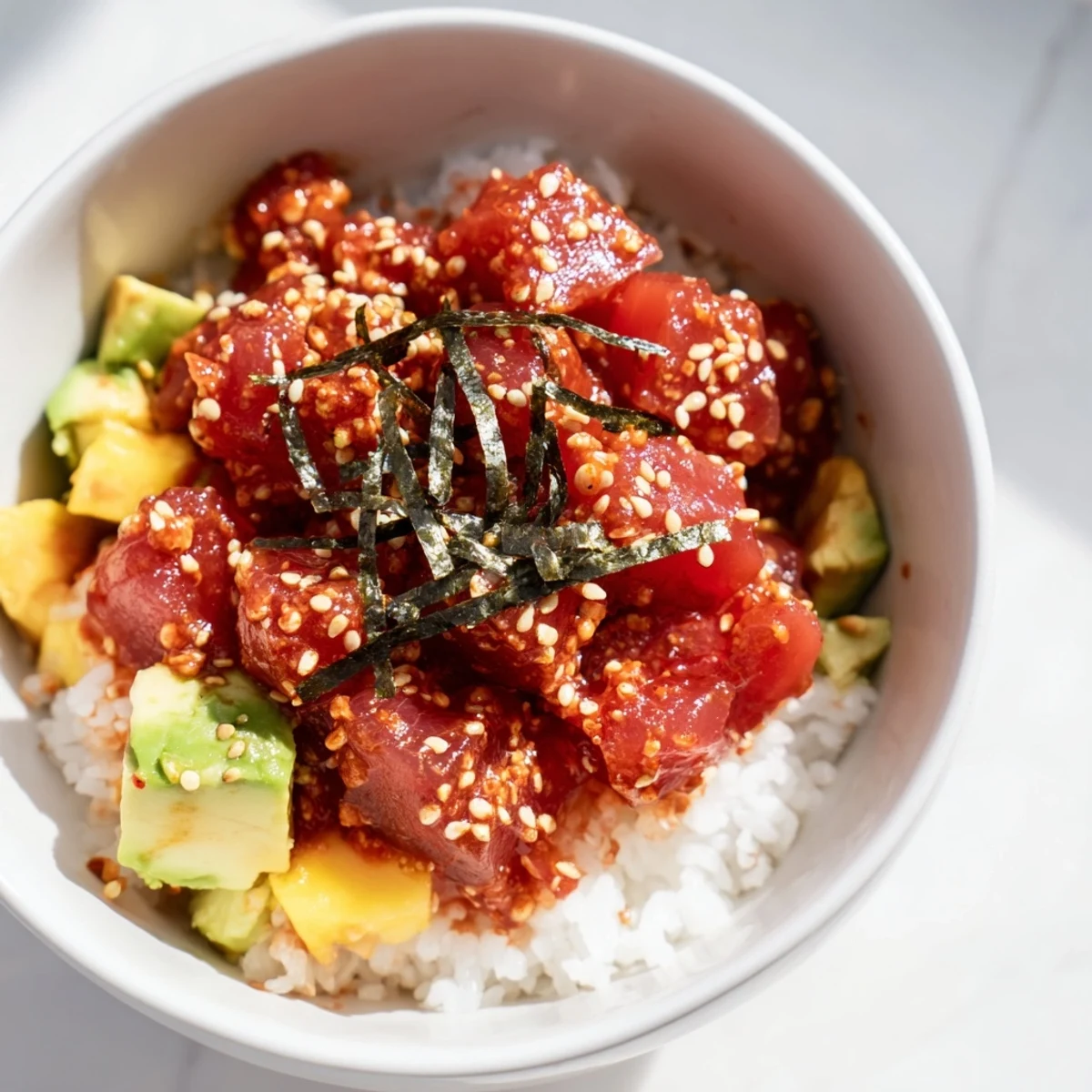 Deconstructed Spicy Tuna Poke Bowl with Avocado and Mango showcasing fluffy rice, nori strips, and sesame seeds.