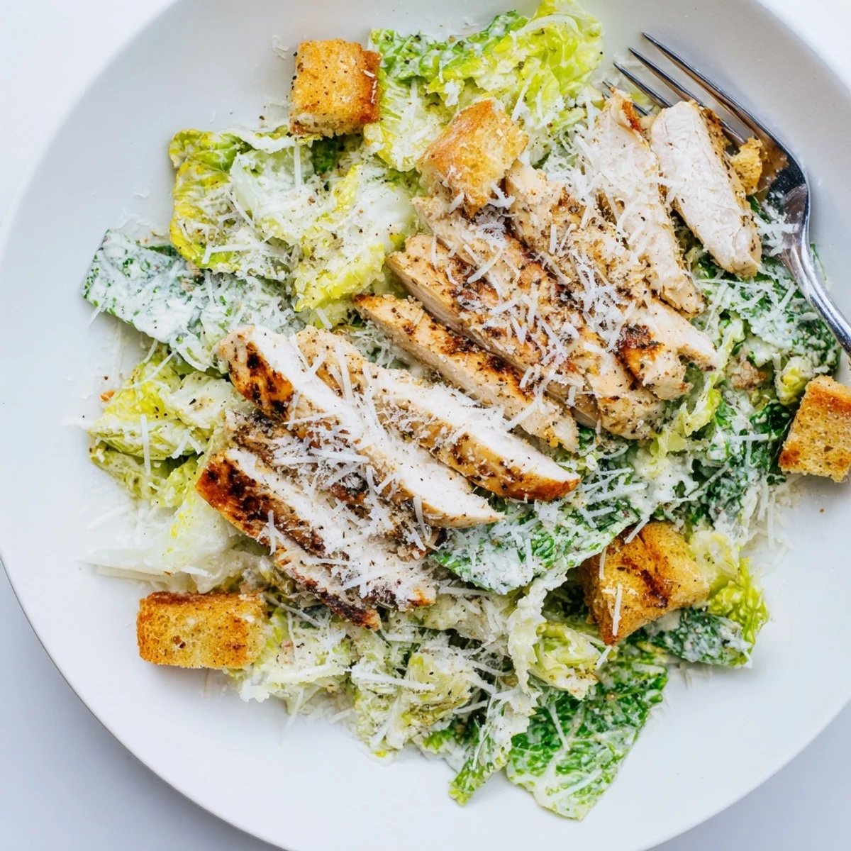 Golden grilled chicken slices rest atop crisp romaine lettuce, creamy Caesar dressing, and crunchy homemade croutons.  