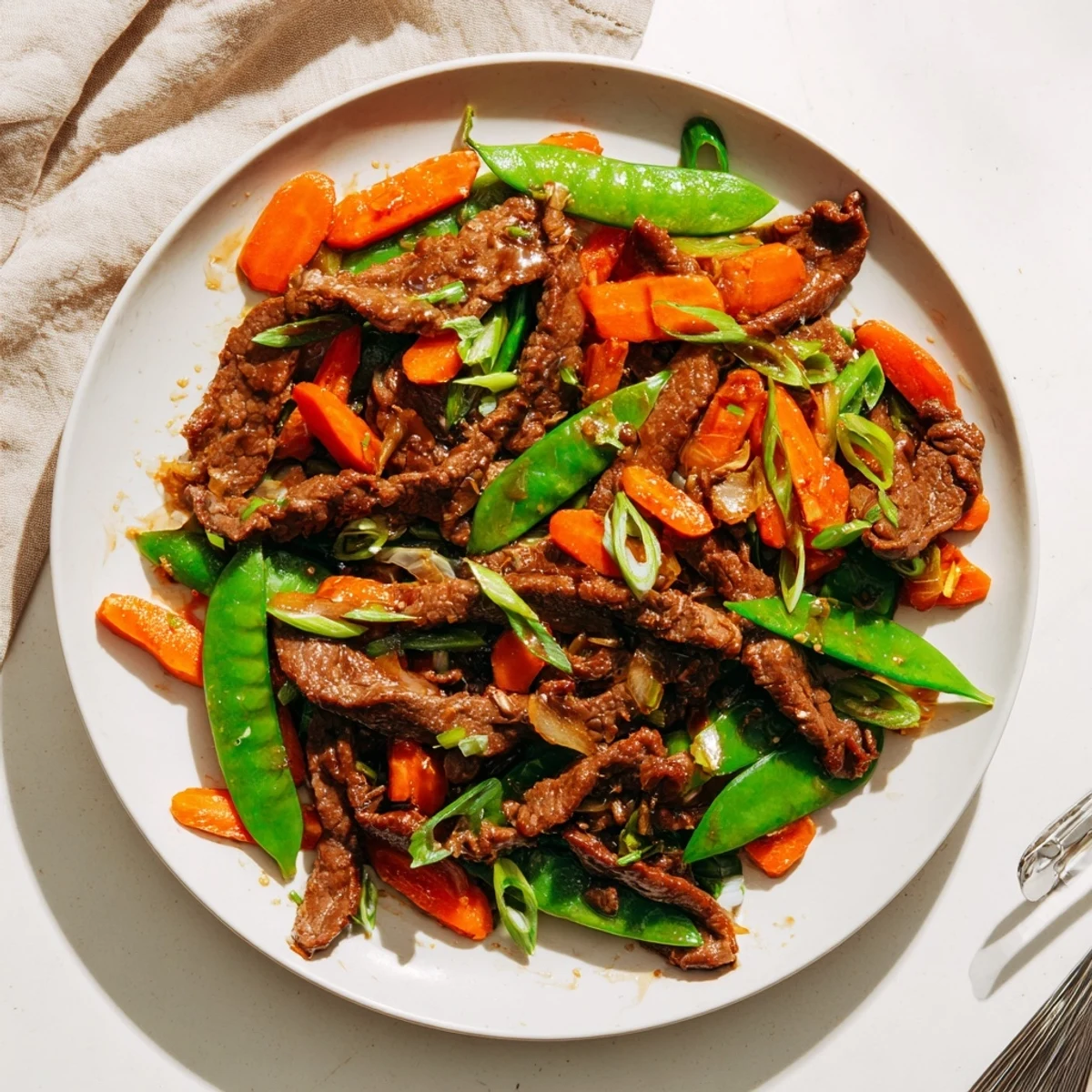 Tender beef, crisp snow peas, and bright carrots coated in a glossy savory stir fry sauce, served hot over steamed rice.