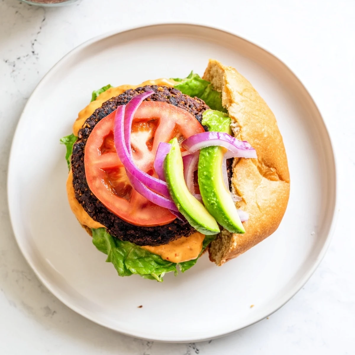 A close-up of a Vegan Black Bean Burger with Chipotle Mayo on a toasted bun, topped with fresh lettuce, tomato, and avocado slices for a vibrant, appetizing meal.  
