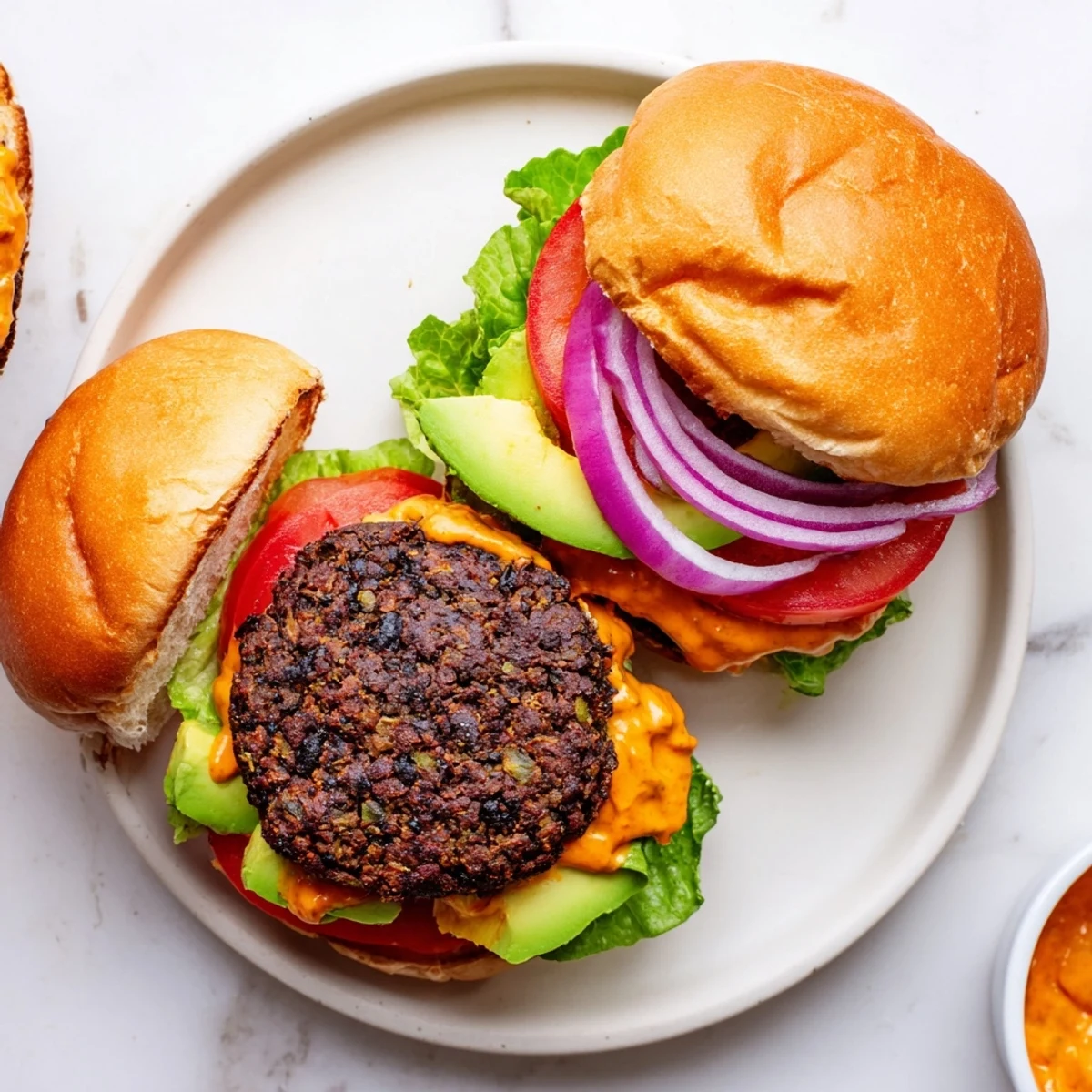 Stacked Vegan Black Bean Burger with Chipotle Mayo on a rustic plate, garnished with red onion and cilantro, served alongside crispy sweet potato fries.  