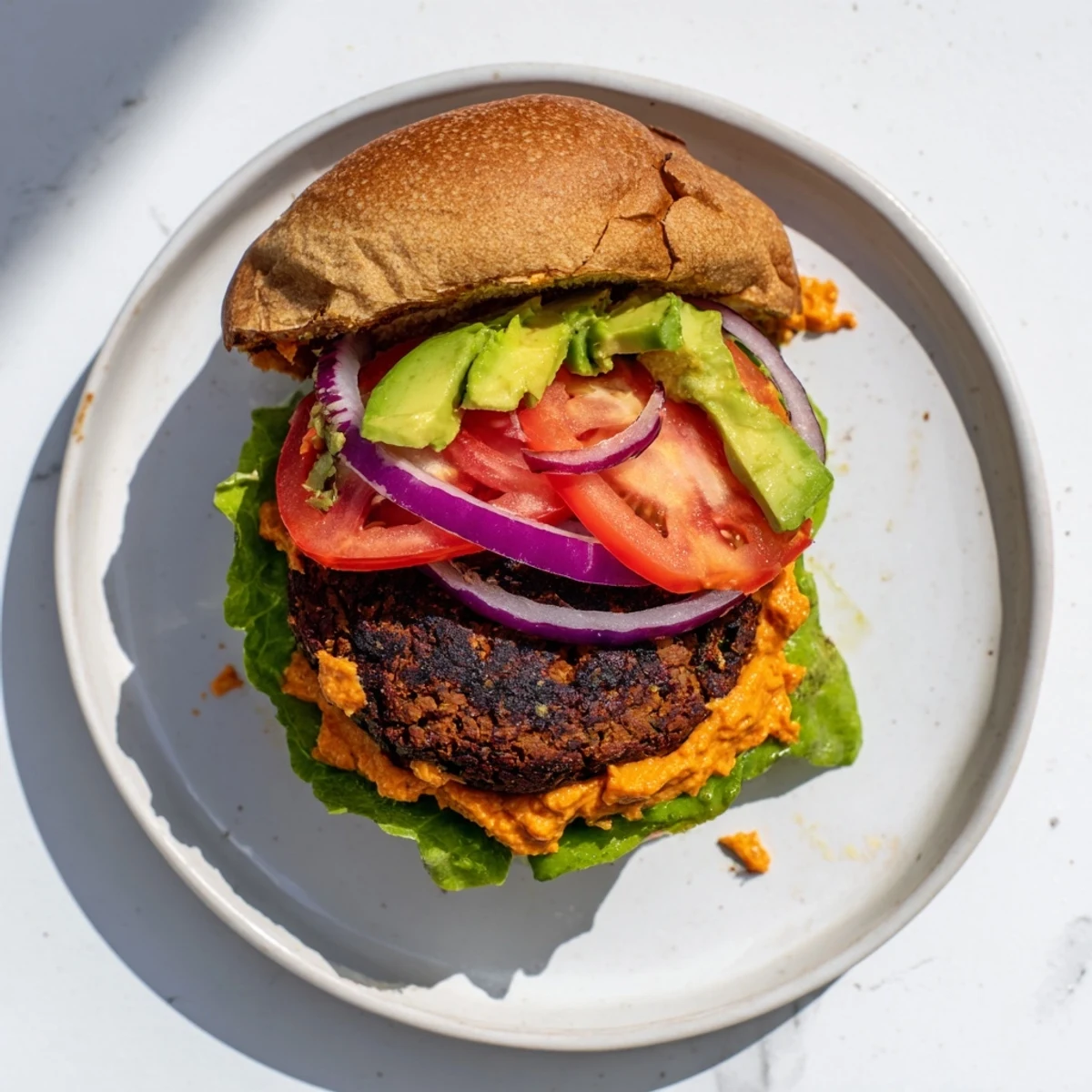 Perfectly cooked Vegan Black Bean Burger patty with a golden crust, smothered in spicy chipotle mayo and layered with colorful veggies on a soft bun.