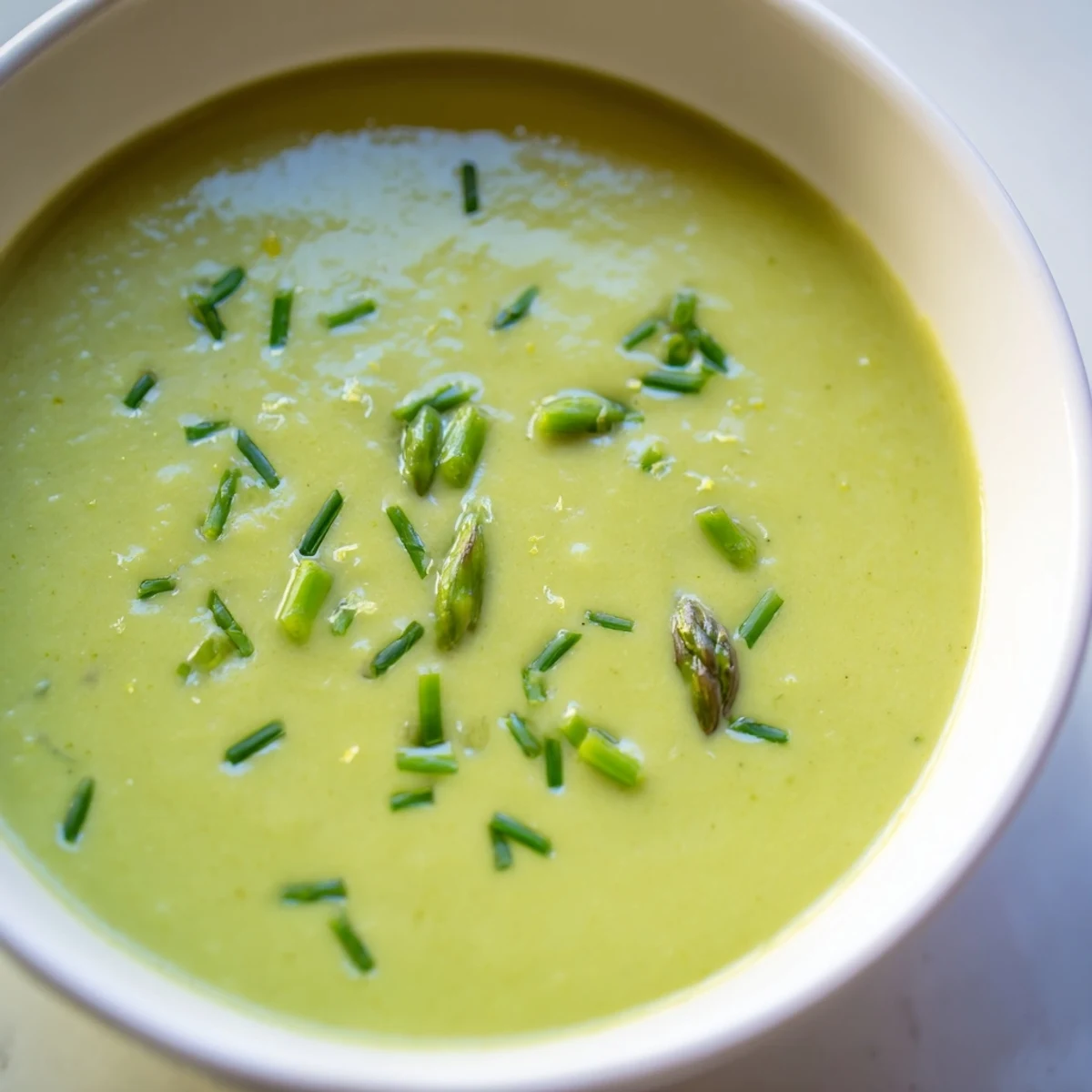 Close-up of creamy asparagus soup with lemon zest, steam rising from the vibrant green puree.  