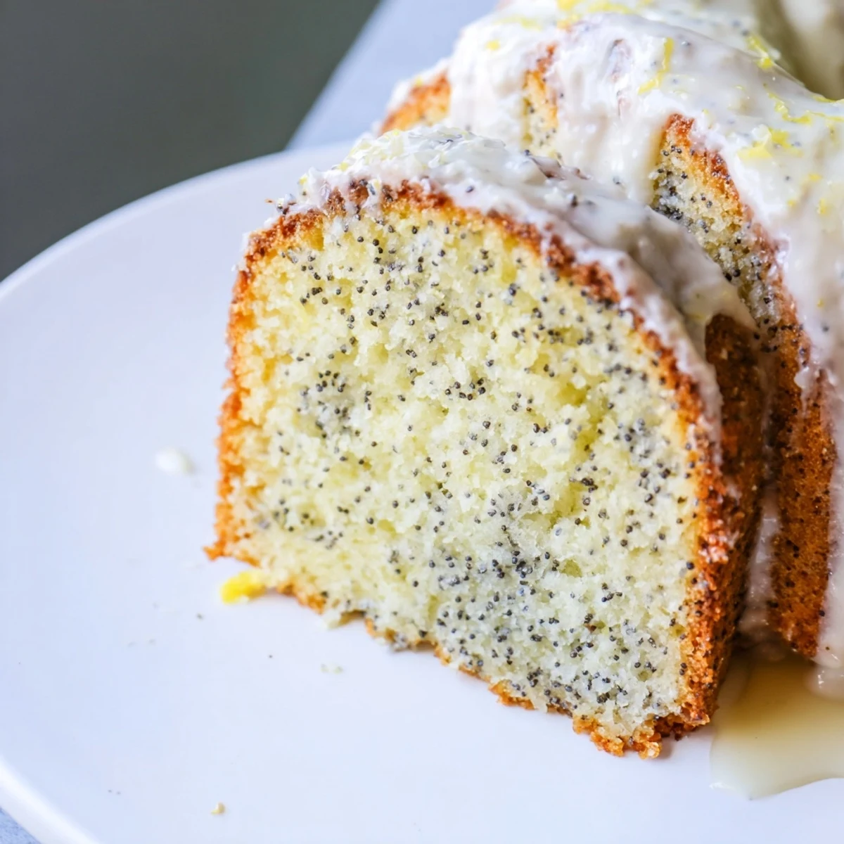 A freshly glazed Lemon Poppy Seed Bundt Cake sits on a cooling rack, the tangy lemon icing dripping down the ridges of the pan.