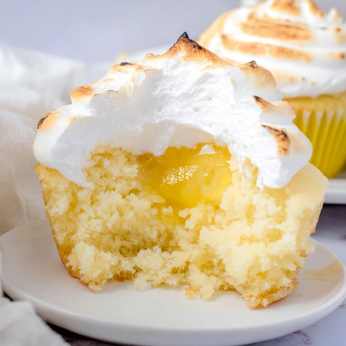 Toasted meringue swirls crown the Lemon Meringue Cupcakes, their golden peaks standing tall and billowy against a rustic backdrop.