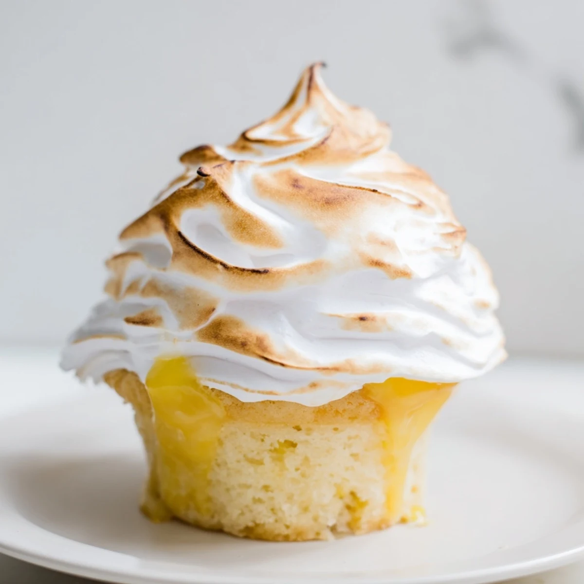Golden-brown Lemon Meringue Cupcakes displayed on a rustic wooden board topped with fresh lemon zest.