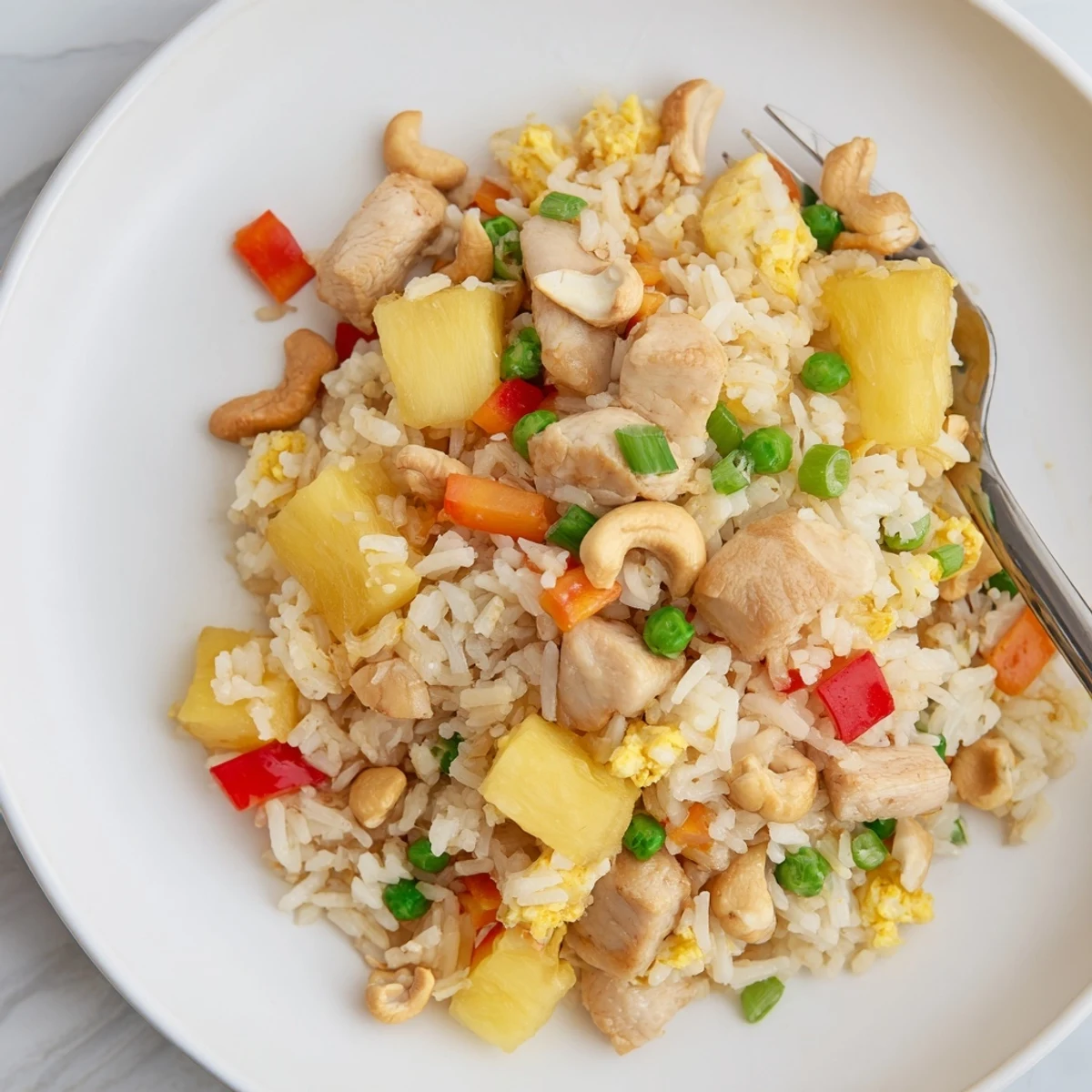 Wok-seared Pineapple Chicken Fried Rice with Cashews is plated in a bowl with peas and carrots for color.