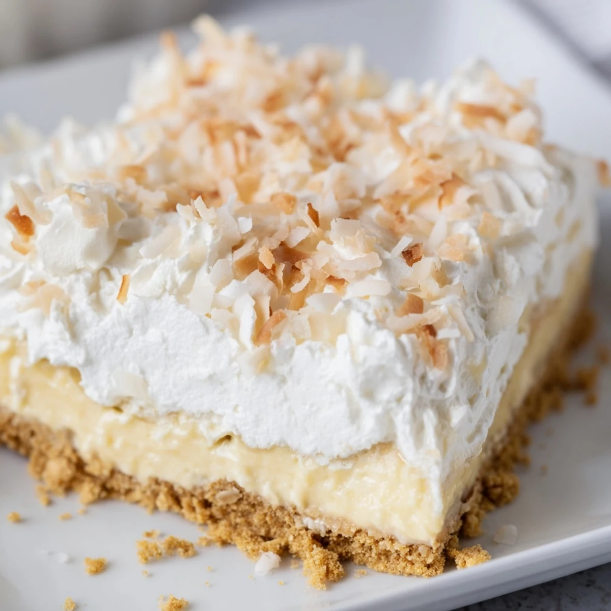 A slice of Coconut Cream Dream Bars reveals a golden graham cracker crust and fluffy whipped cream topping.