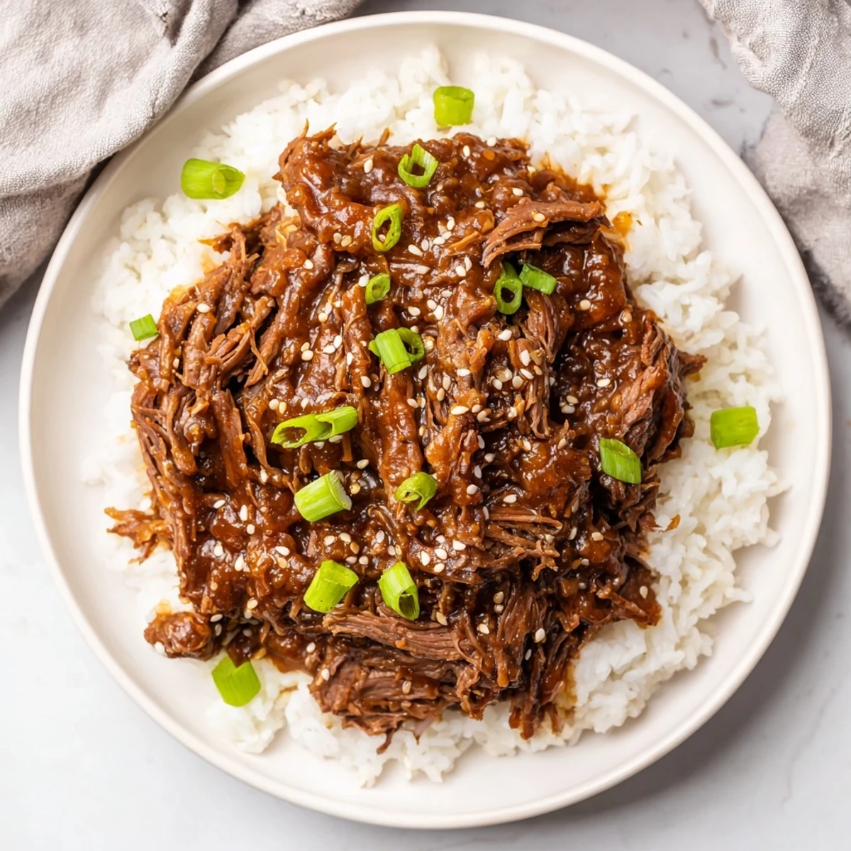 Close-up of tender Crock Pot Korean Beef with glossy savory-sweet sauce, served over fluffy white rice with green onions and sesame seeds.