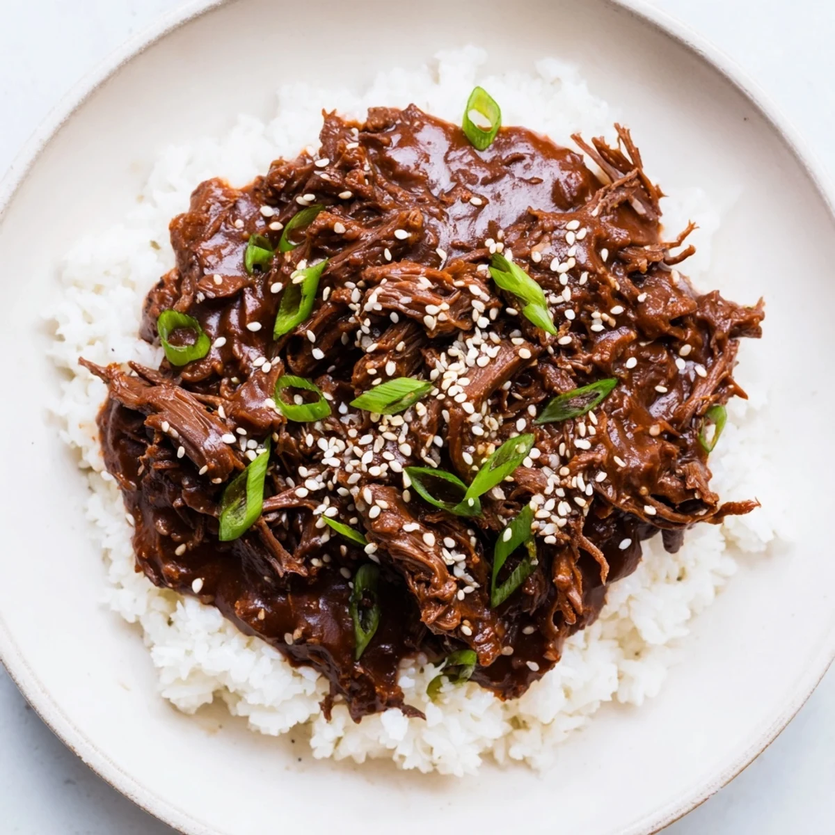 Family-style serving of Crock Pot Korean Beef piled on jasmine rice, garnished with sesame seeds and scallions, perfect for an easy weeknight dinner.