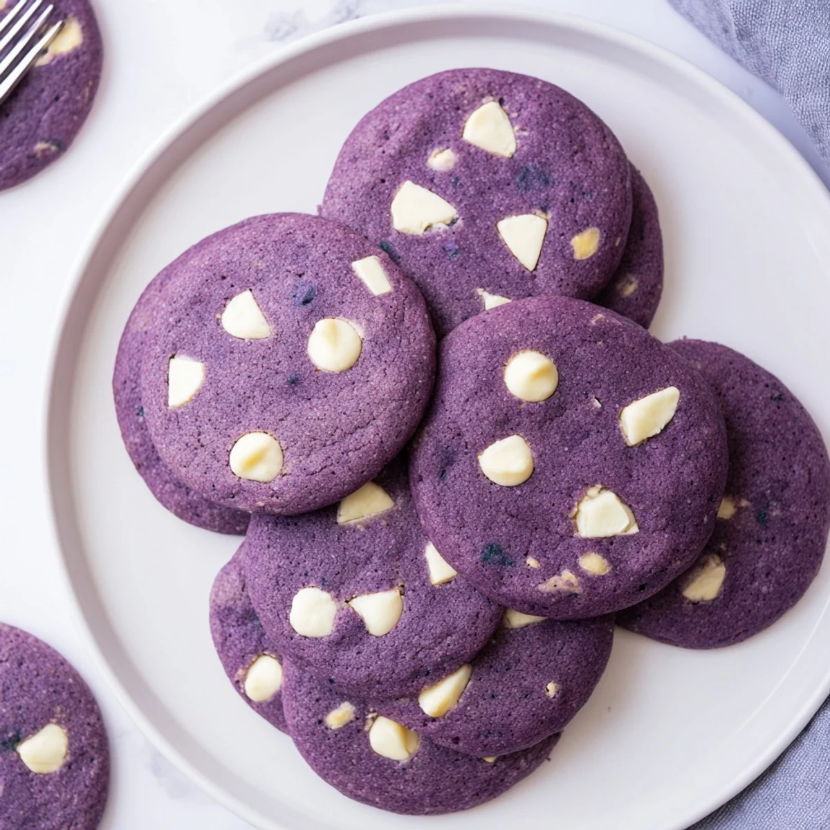 Warm White Chocolate Ube Cookies with soft centers and chewy edges, studded with creamy white chocolate chips on a baking sheet.