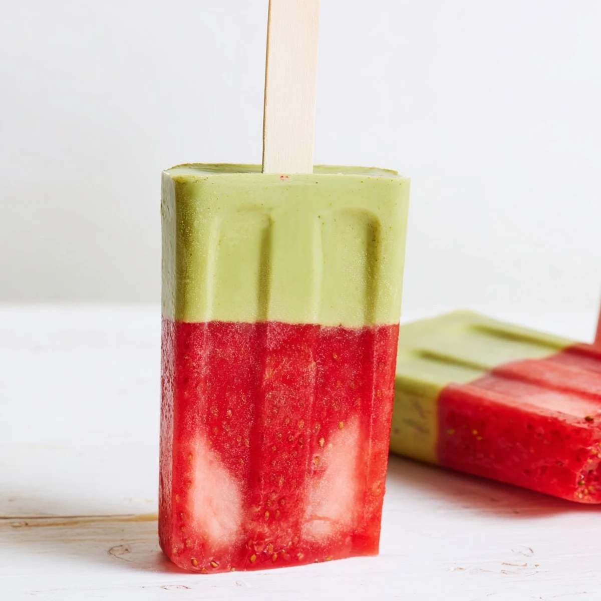 Vibrant pink and green striped Strawberry Matcha Latte Popsicles resting in a popsicle mold, showcasing creamy layers perfect for a cool summer dessert.