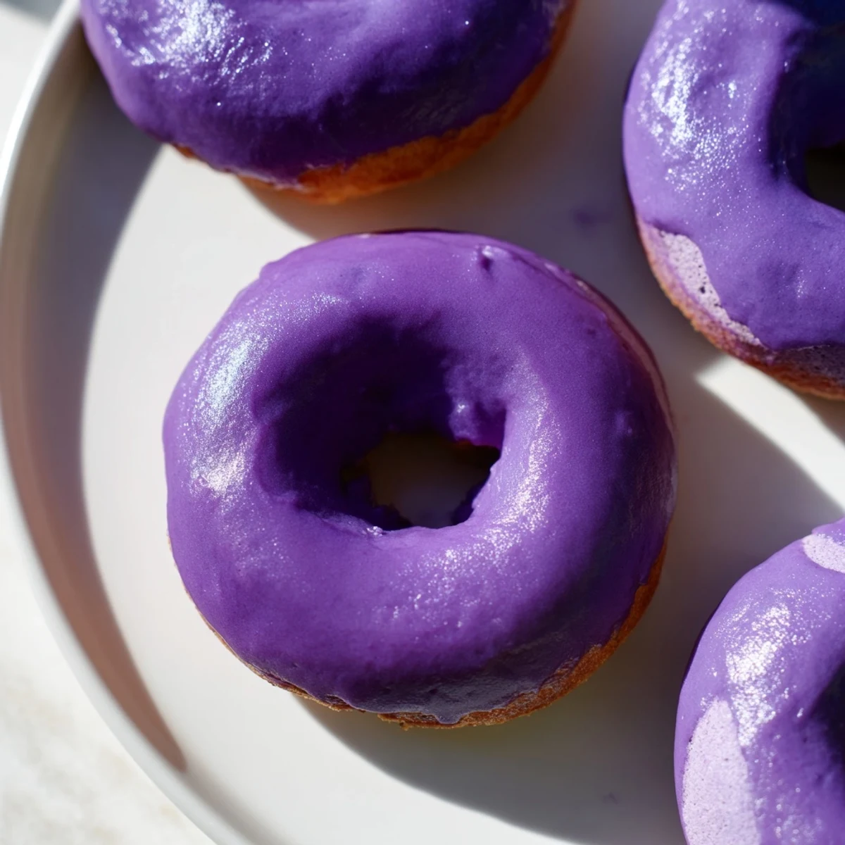 Freshly fried Ube Mochi Donuts coated in a vibrant purple glaze, ready to serve with a hot cup of coffee.
