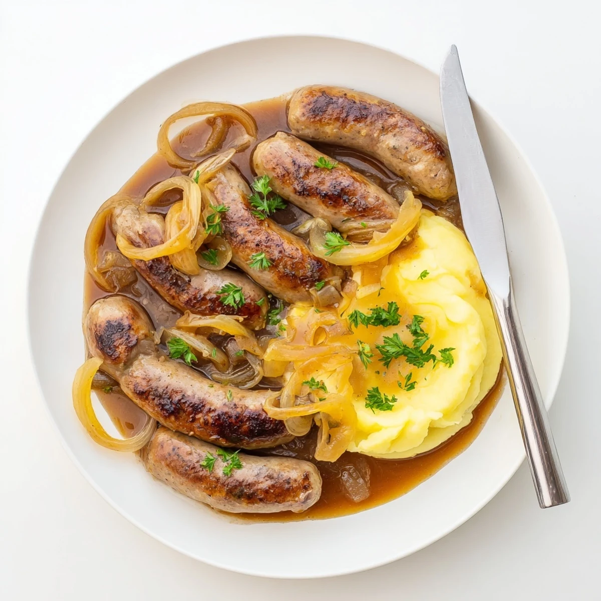 Golden-brown sausages simmering in rich onion gravy over creamy mashed potatoes, a cozy British classic.