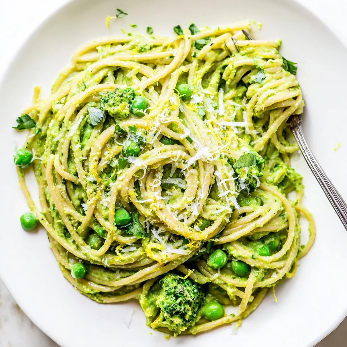 A close-up of Veggie Smuggler Avocado Pasta with creamy green sauce coating whole wheat spaghetti, topped with steamed broccoli and peas.