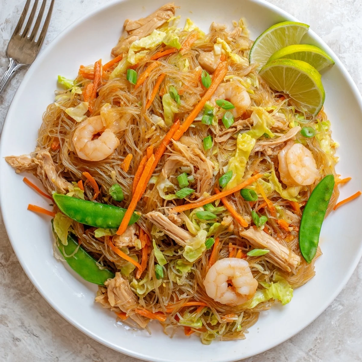 Golden plate of Traditional Pancit Bihon piled high with tender rice noodles, chicken, shrimp, and colorful julienned vegetables