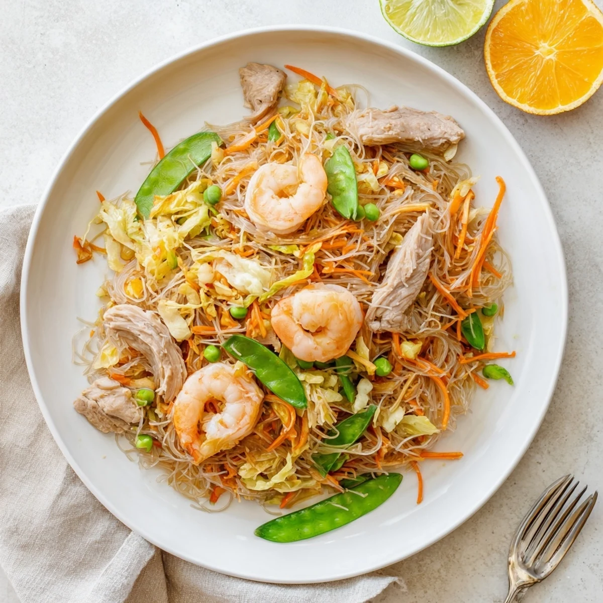 Steaming bowl of savory Traditional Pancit Bihon featuring translucent rice noodles stir-fried with chicken, shrimp, and crisp cabbage