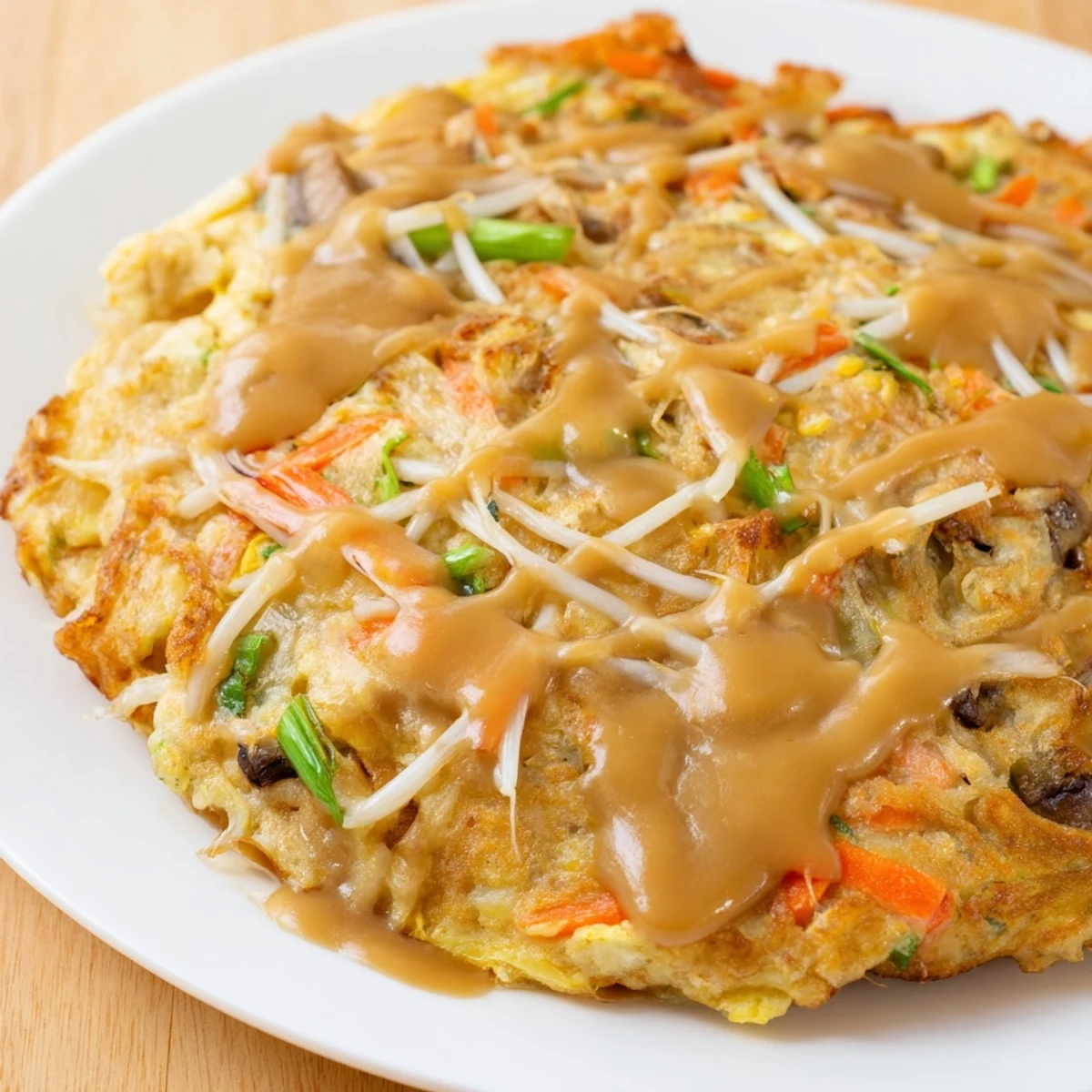 Golden crispy Egg Foo Young patties drizzled with rich brown gravy on a white plate