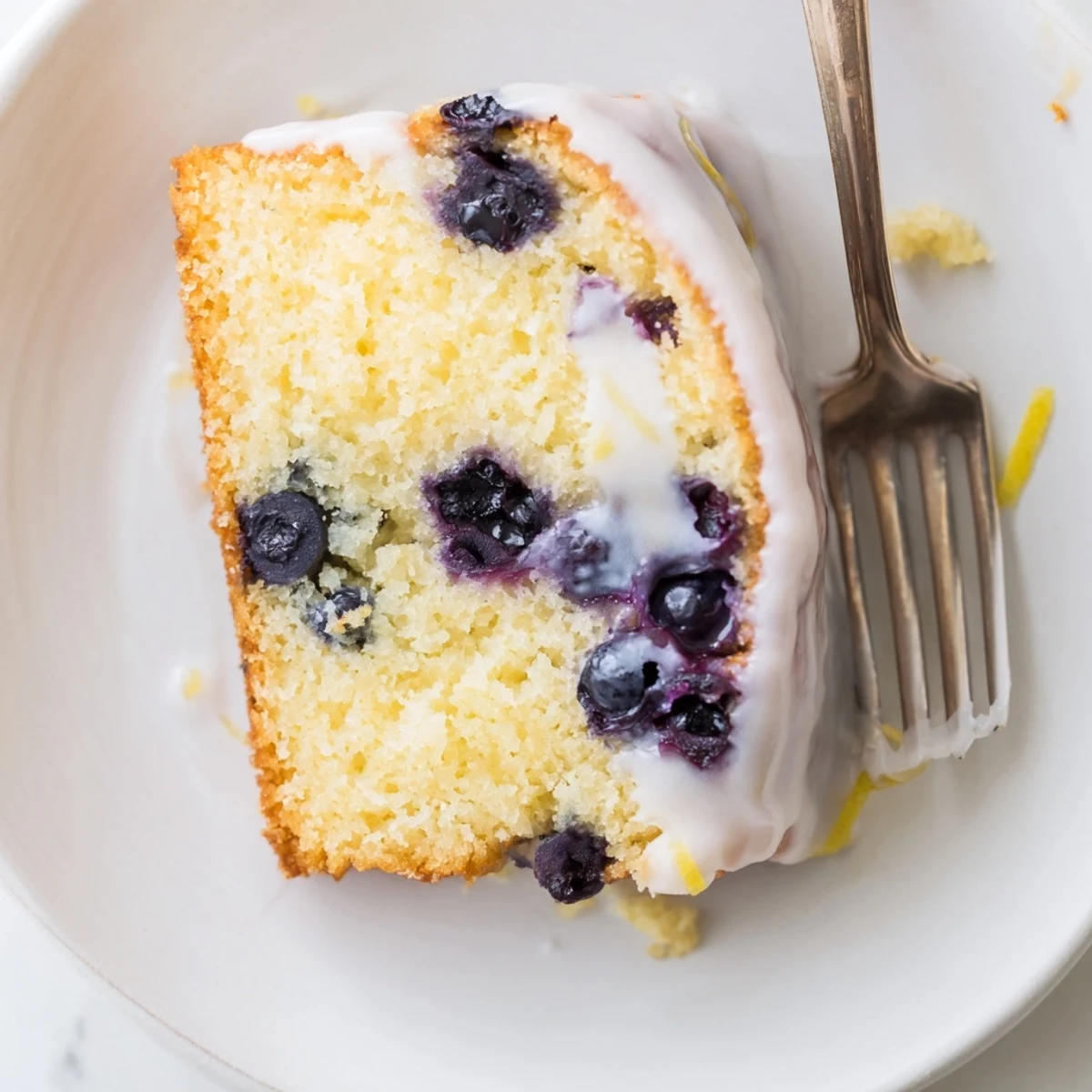 Slice of moist lemon blueberry cake showing purple berries and zesty lemon glaze