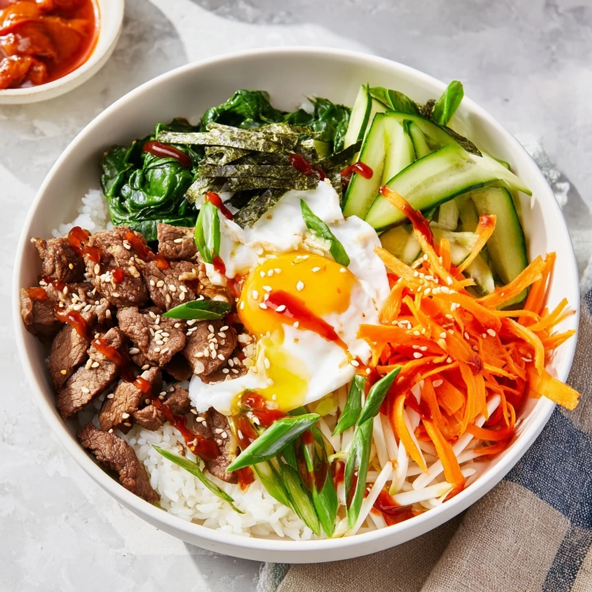 Golden fried egg tops Korean-inspired breakfast bowl with marinated beef and fresh vegetables over steamed white rice