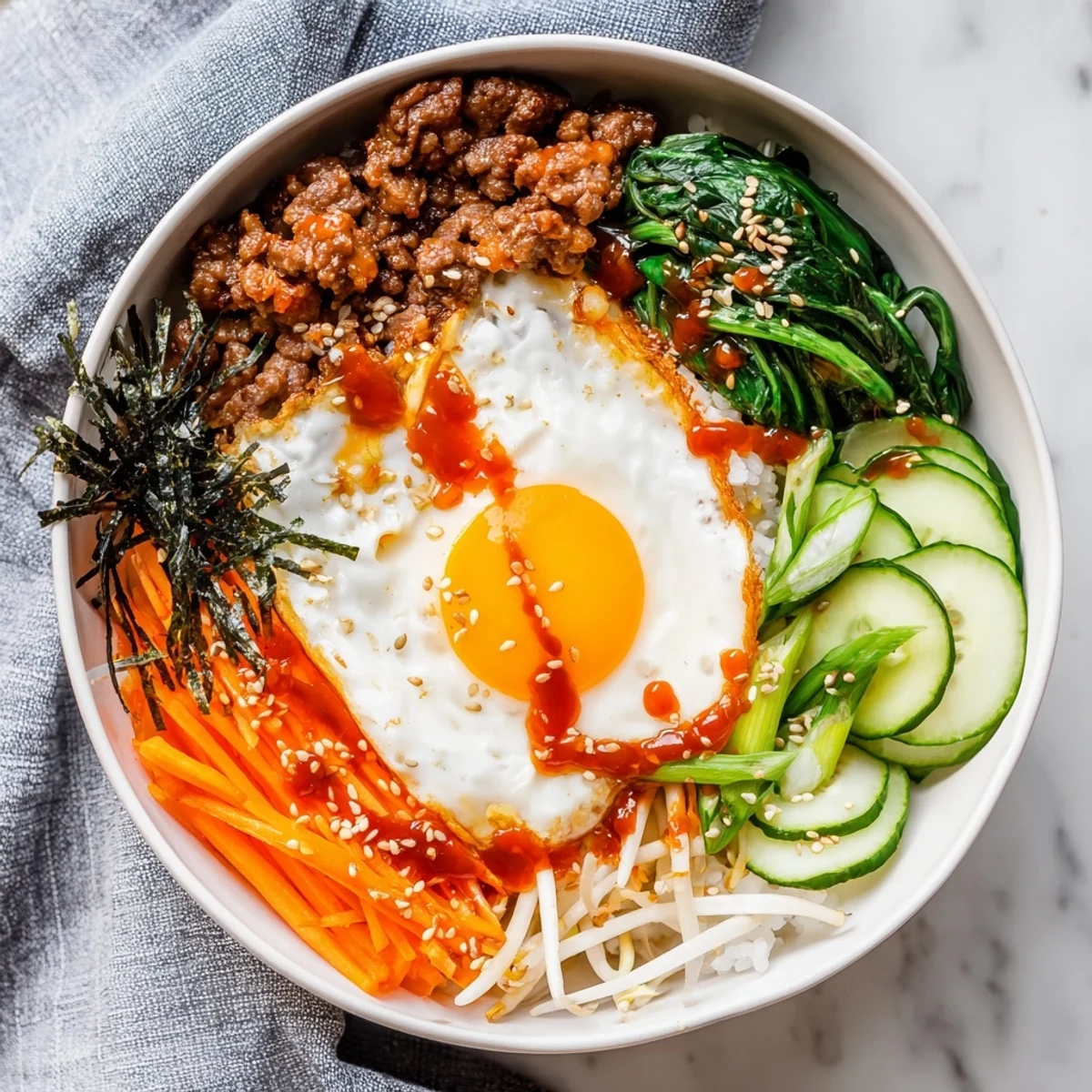 Spicy gochujang drizzled over Korean-inspired breakfast bowl with tender beef, fried egg, and crisp vegetable garnish