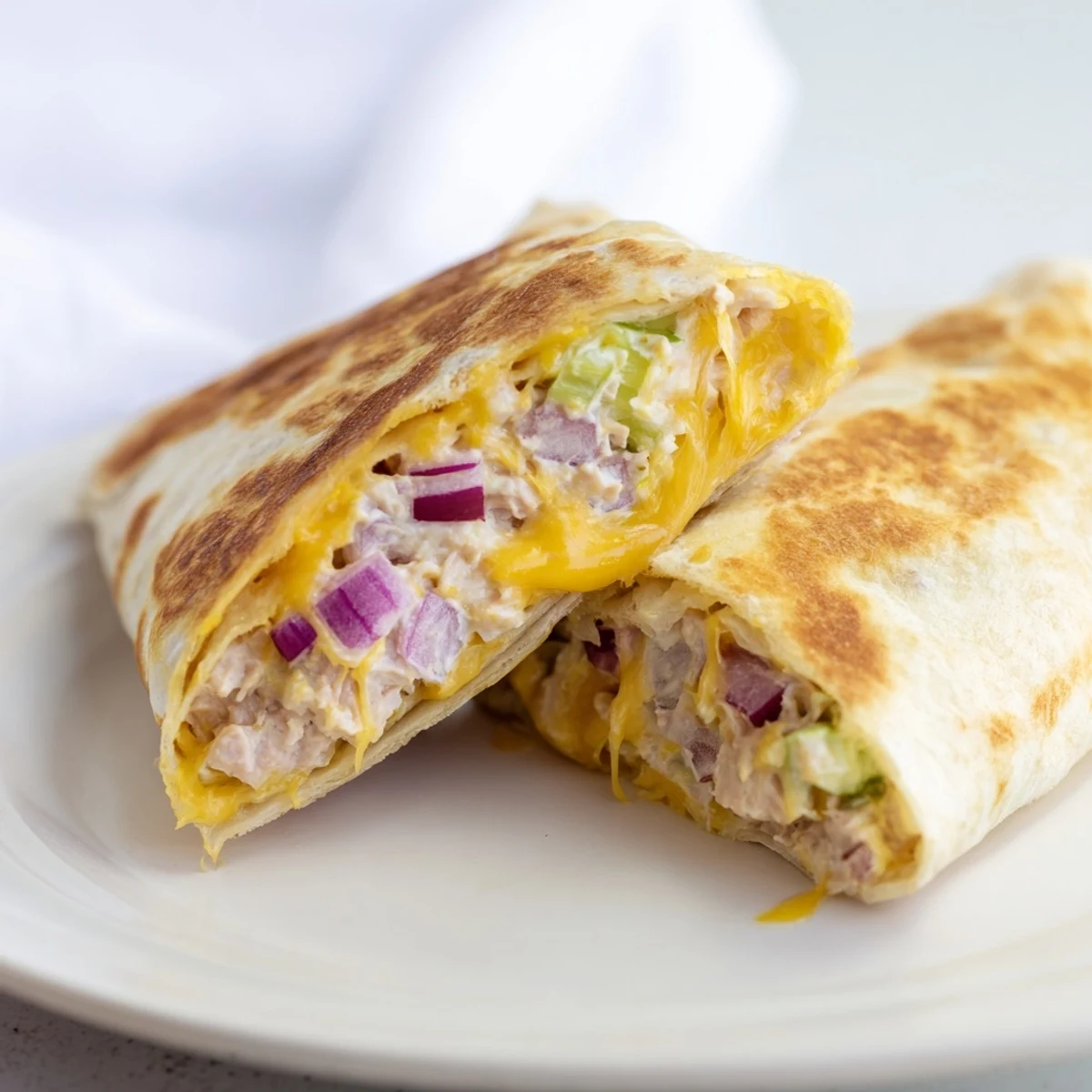 Golden grilled Tuna Melt Wrap sliced in half revealing melted cheddar and creamy tuna filling