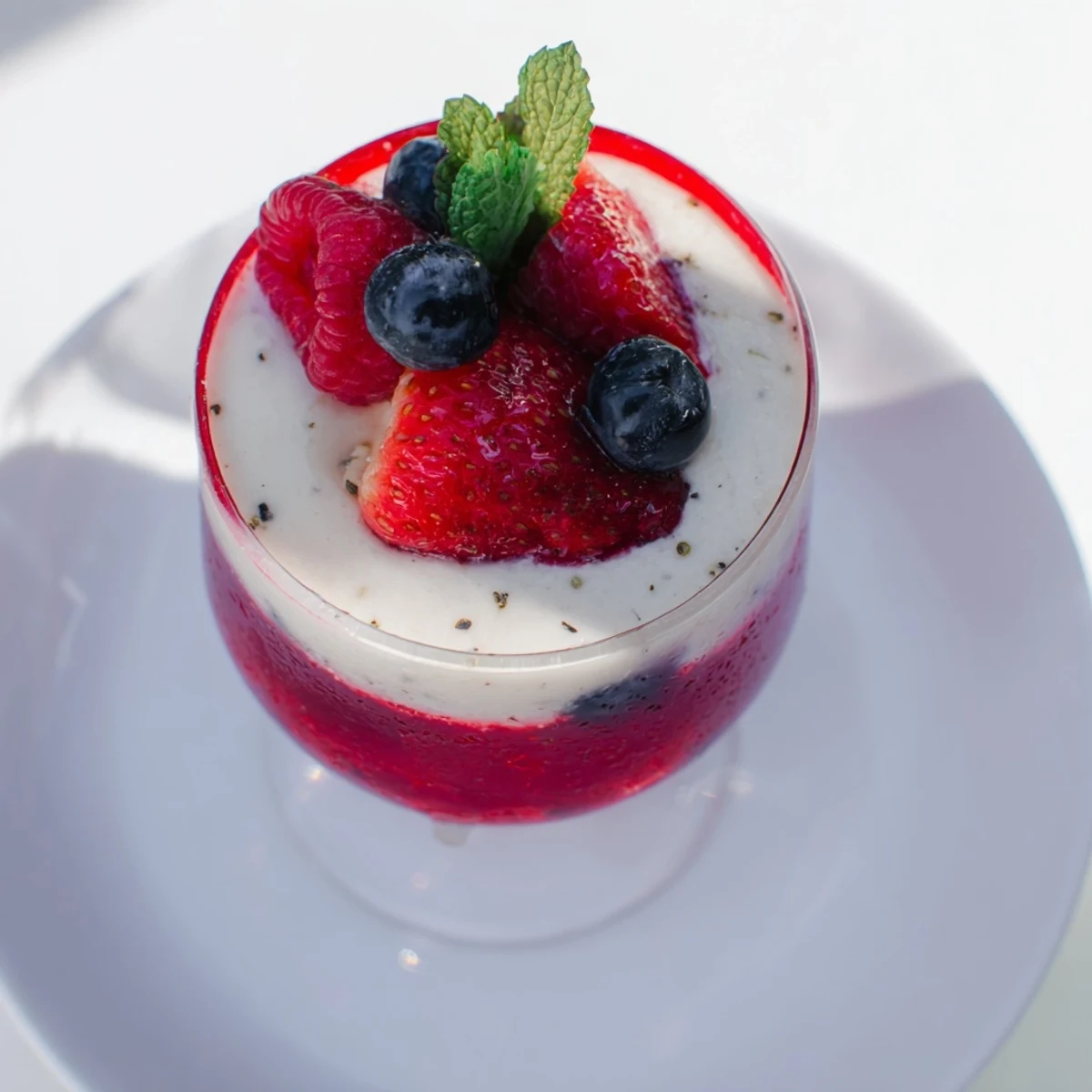 Creamy vanilla mousse layered over vibrant red berry jello in clear parfait glasses topped with mint