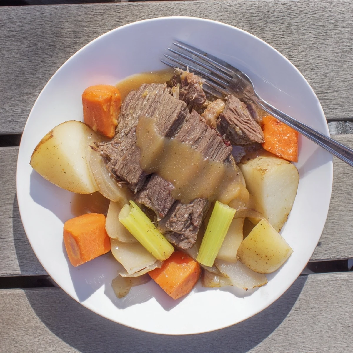 Fork-tender Southern style pot roast nestled beside roasted vegetables and drizzled with savory homemade gravy on a white serving platter.