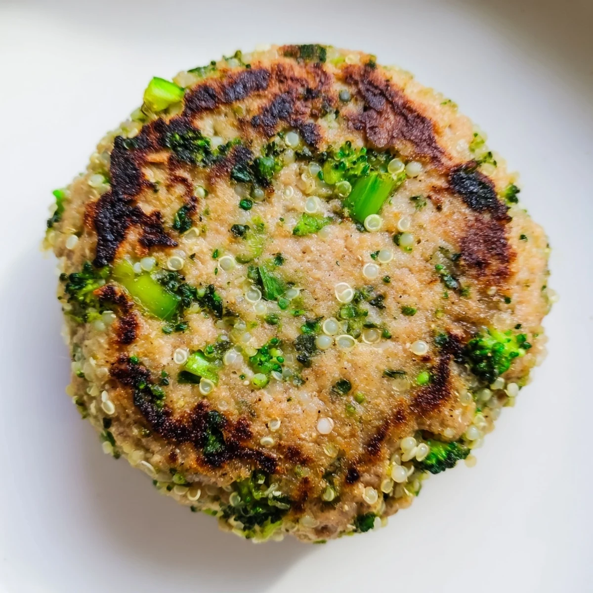 Golden brown turkey broccoli and quinoa burgers sizzling in a skillet with fresh green onion garnish