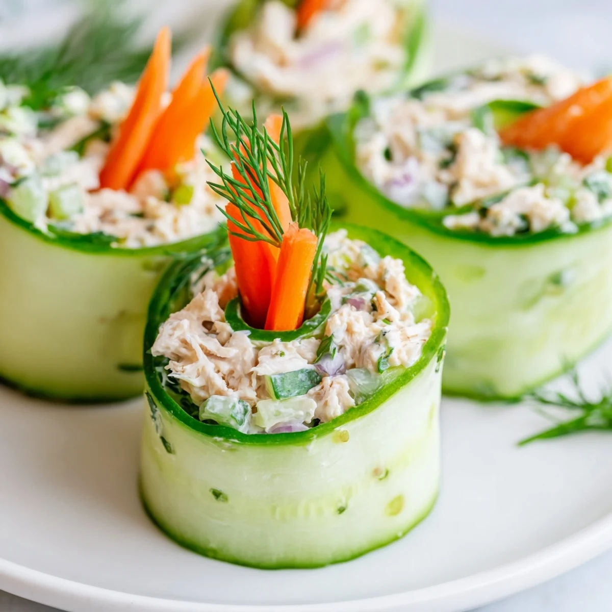 Fresh chicken salad cucumber roll ups filled with creamy herb chicken on crisp green cucumber ribbons arranged on a white serving platter