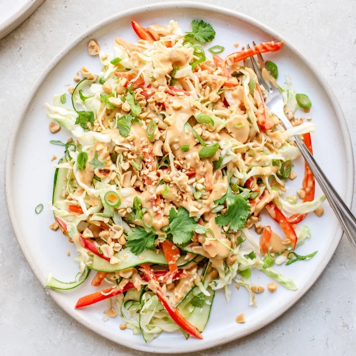 Colorful Thai salad peanut sauce featuring crisp cabbage, carrots, and cucumber drizzled with creamy dressing
