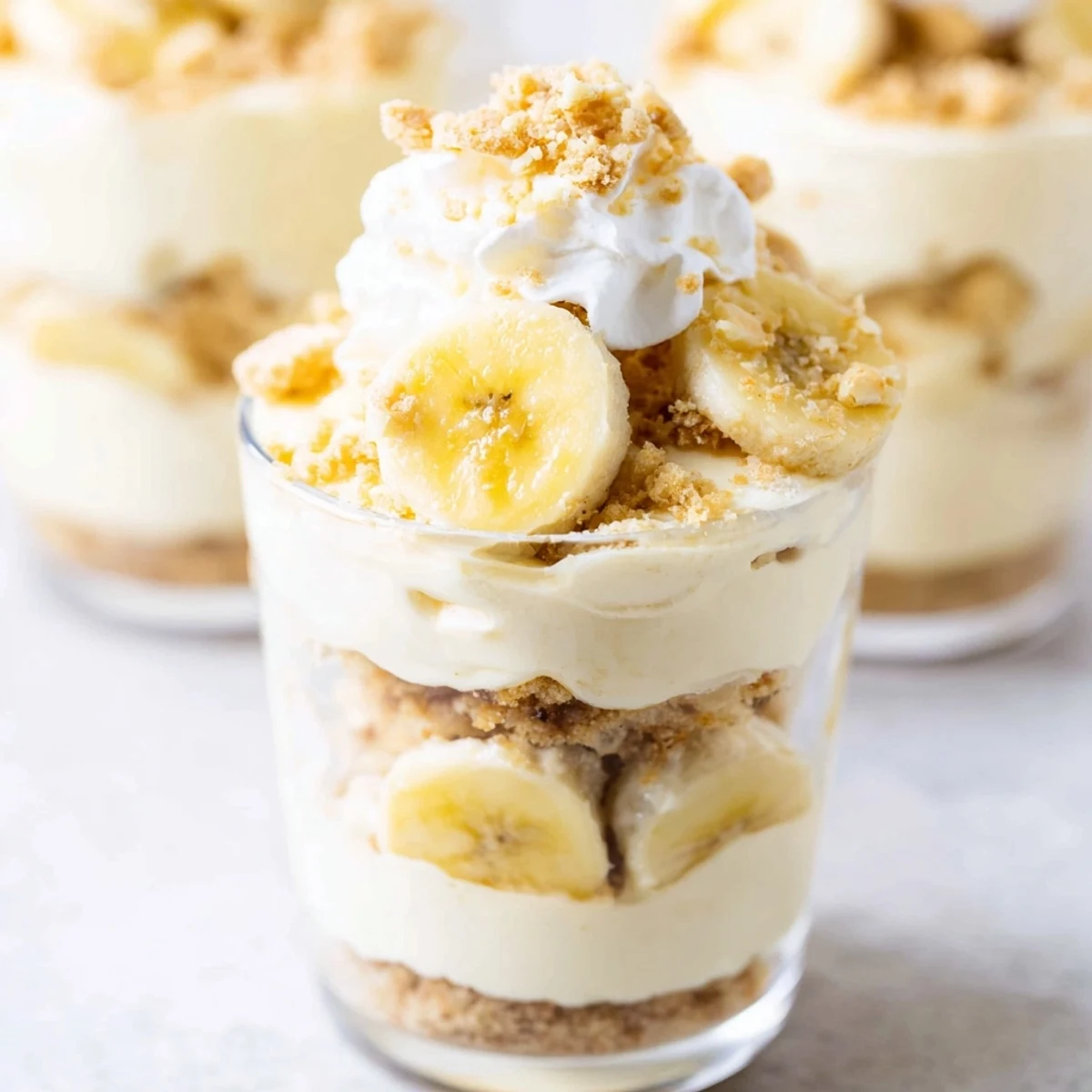 Creamy No Bake Banana Pudding Cheesecake Cups topped with fresh banana slices and vanilla wafer crumbs