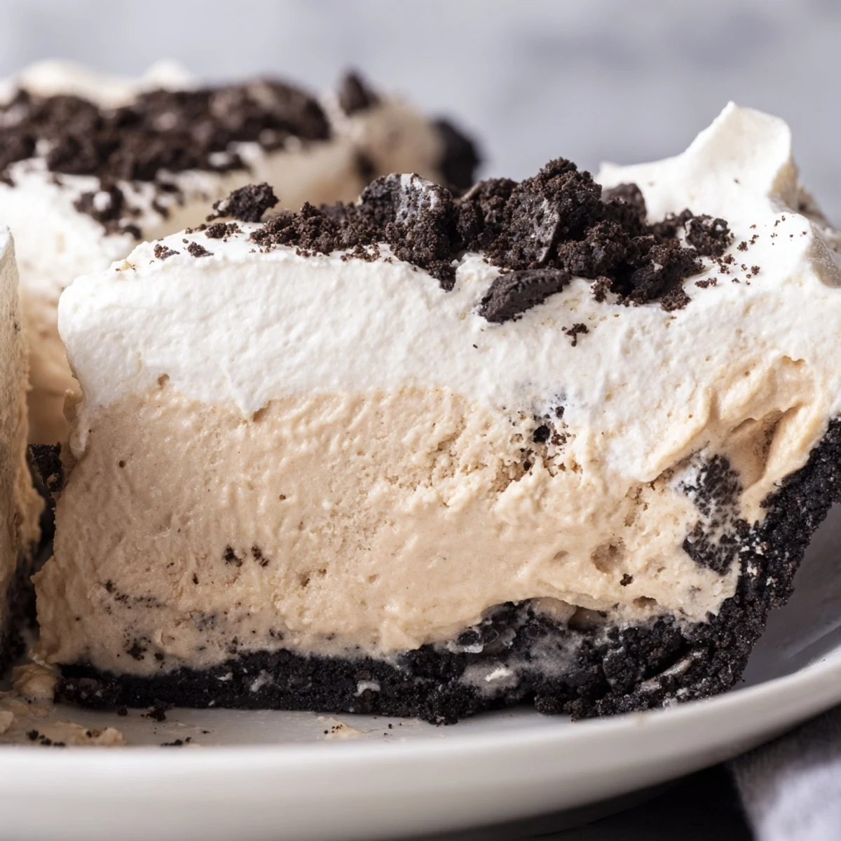 Creamy Peanut Butter Oreo Pie slice with fluffy whipped topping and chocolate cookie crumbles on a dessert plate