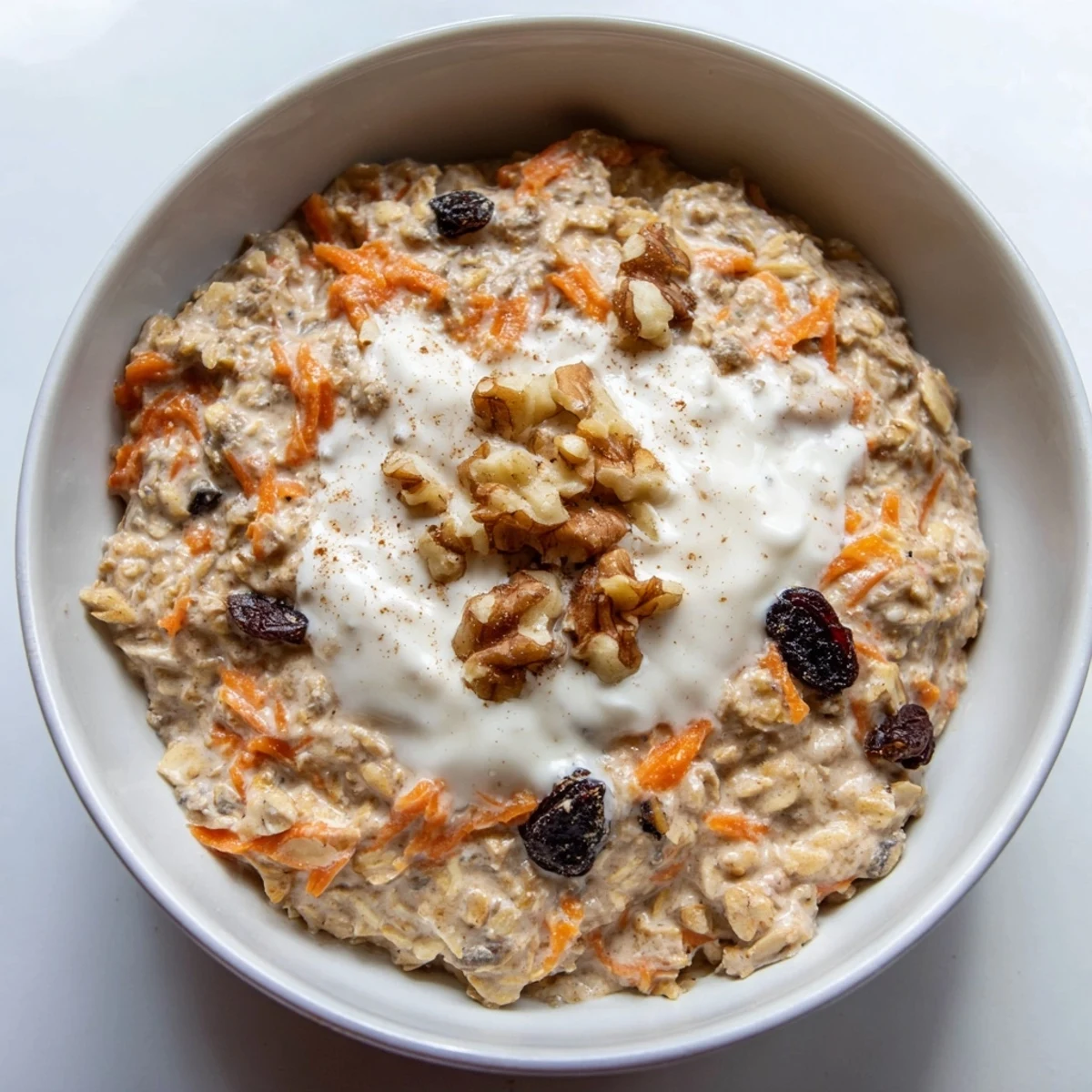 Carrot cake overnight oats with visible grated carrots, plump raisins, and chopped pecans in a glass bowl