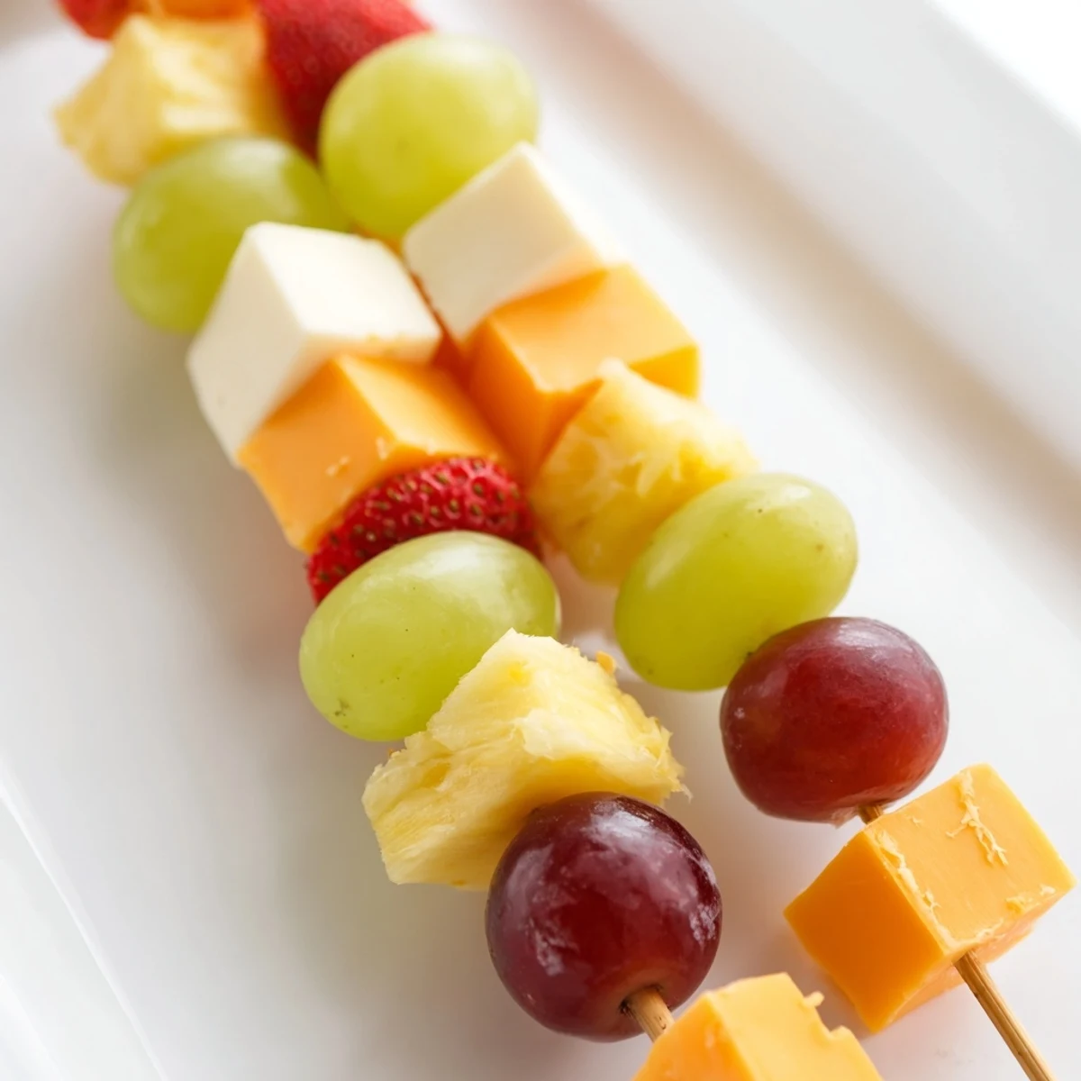 Colorful fruit and cheese kabobs arranged on a platter with red grapes, pineapple, and cheddar cubes