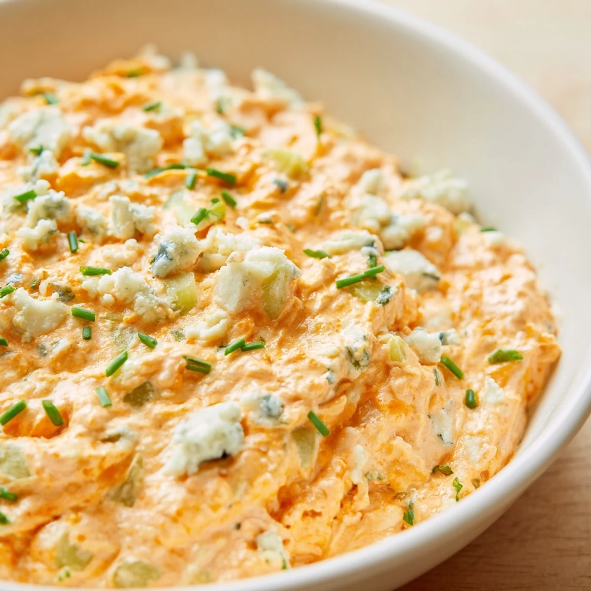 Creamy buffalo pickle dip in a serving bowl surrounded by crispy chips and fresh veggie sticks for dipping