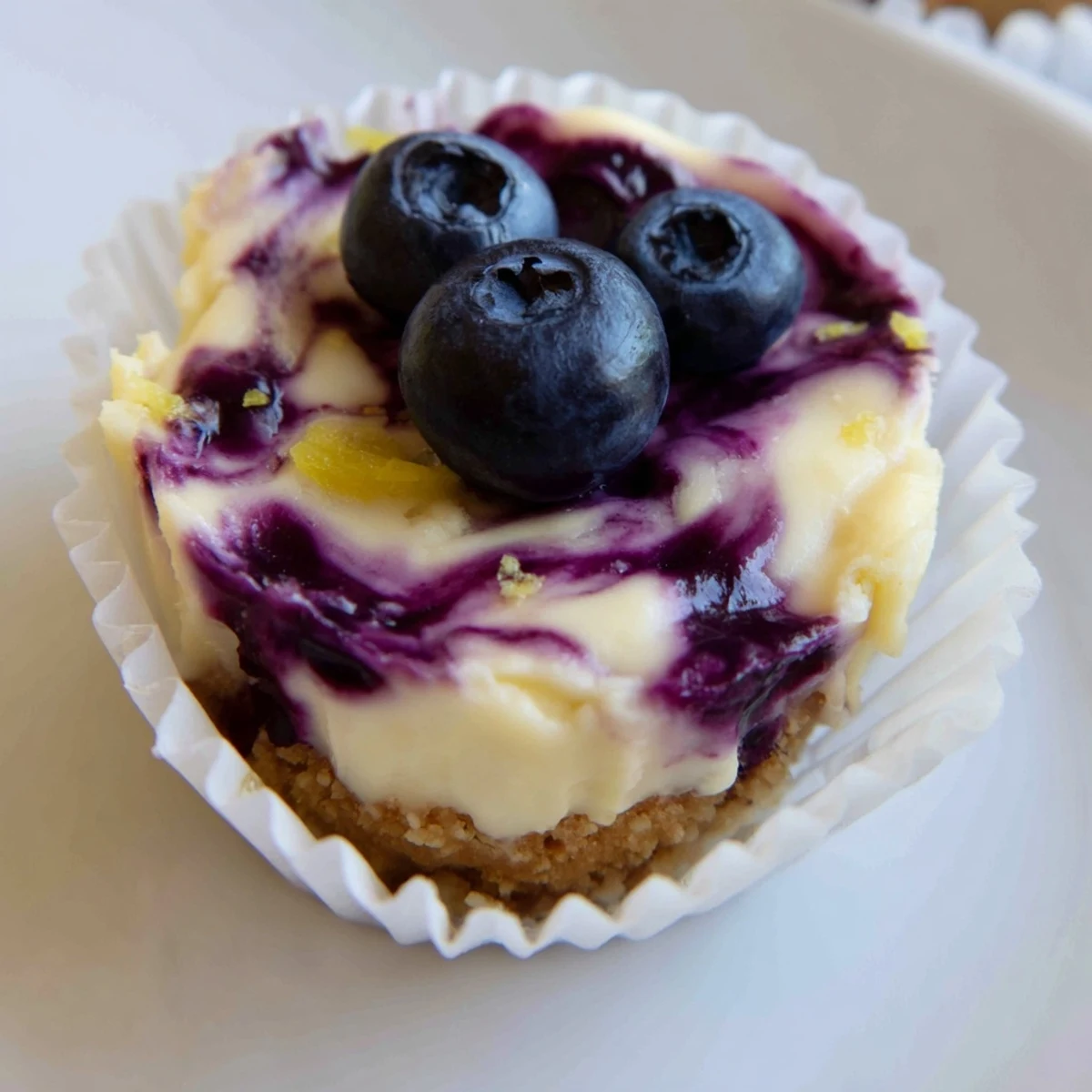 Bite-sized mini lemon blueberry cheesecakes garnished with fresh berries and bright lemon zest curls