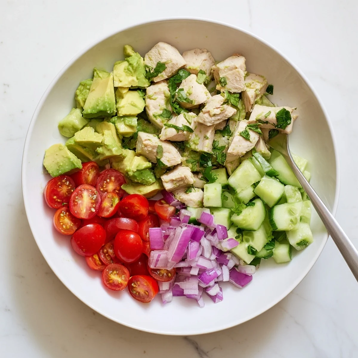 Colorful bowl of healthy avocado chicken salad with juicy grilled chicken chunks, diced fresh avocados, cherry tomatoes, cucumber, and cilantro tossed in zesty lime dressing