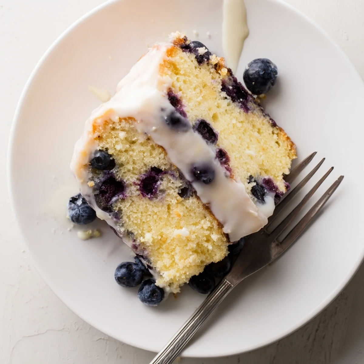 Moist lemon blueberry cake drizzled with white glaze and topped with fresh berries