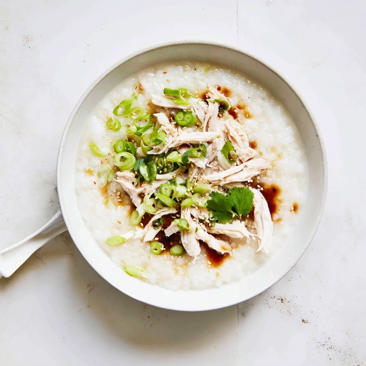 Steaming hot chicken congee with shredded chicken and fresh cilantro garnish on white background