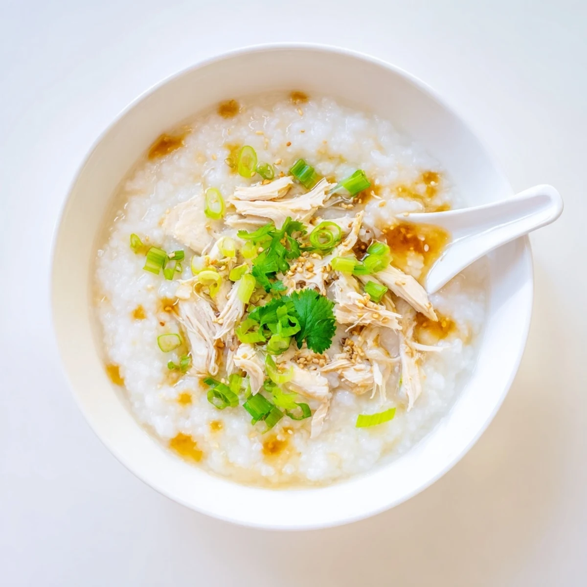 Creamy chicken congee topped with scallions and drizzled sesame oil in a bowl