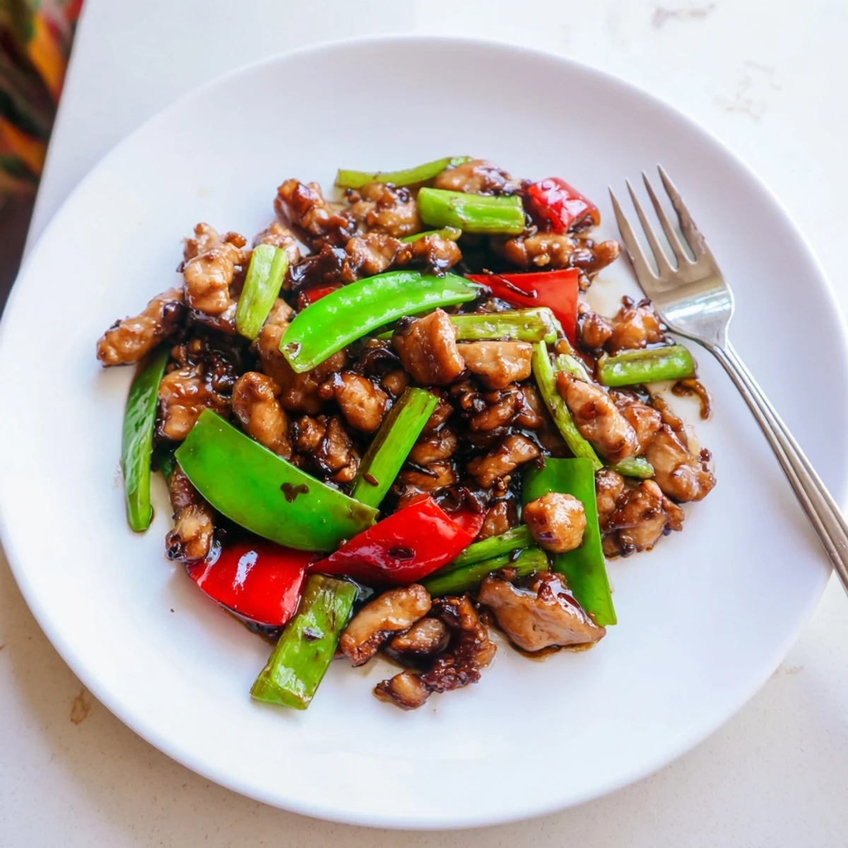 Glossy stir fried Chinese garlic chicken with crisp bell peppers and snow peas