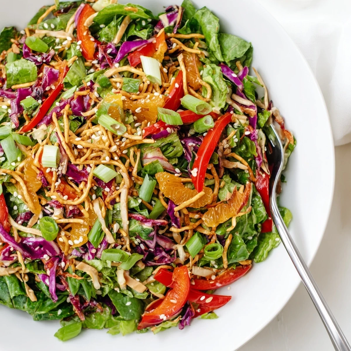 A vibrant Mandarin Sesame Crunch Salad in a large bowl drizzled with tangy sesame ginger dressing.